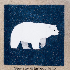 Pode incluir: Uma aplicação de urso polar branco em um tecido azul escuro com um padrão de estrelas brancas. O texto "Sewn by @turtlequilterjo" está na parte inferior da imagem.