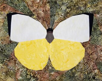 May include: A fabric butterfly quilt block with white and yellow wings, black accents, and a brown body. The background features a batik fabric with green, brown, and cream floral patterns. Text at the bottom reads "Sewn by @sewmliss."