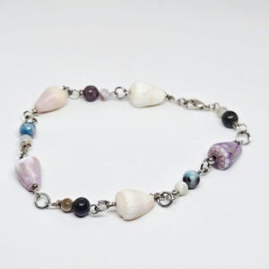 May include: A delicate bracelet featuring a variety of natural elements. The bracelet incorporates cone-shaped seashells in shades of white and pink, interspersed with small, colorful beads. The chain is silver-toned, creating a coastal theme.