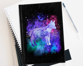 Puede incluir: Una libreta negra con un diseño de galaxia que presenta una silueta de lobo. El lobo está formado por constelaciones y estrellas. La galaxia es una mezcla de colores púrpura, azul y verde con purpurina dorada.