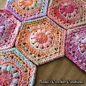 May include: A collection of colourful, handmade crochet hexagon pieces. The pieces feature a floral design in shades of pink, orange, and green. The text "Nana's Crochet Creations" is visible in the bottom right corner.