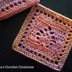 May include: A close-up of a crocheted square with a pink, orange, and yellow ombre color scheme. The square has a lacy pattern with open spaces.