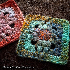 May include: Two crocheted squares, one in shades of pink, orange, and white, and the other in shades of teal, blue, and orange. The squares are made with a textured stitch and have a floral design in the center.