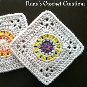 May include: Two crocheted squares with a flower design in the center. The squares are beige with a light brown border. The flower design is made with different colored yarns, including yellow, green, blue, and purple.