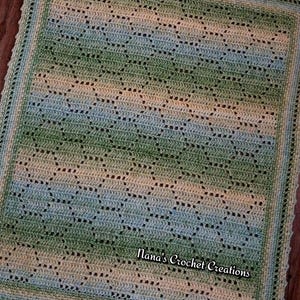 May include: A rectangular crochet blanket featuring a repeating geometric pattern in variegated shades of green, blue, and cream. The blanket has a decorative scalloped border and includes the text Nana's Crochet Creations in the lower right corner.