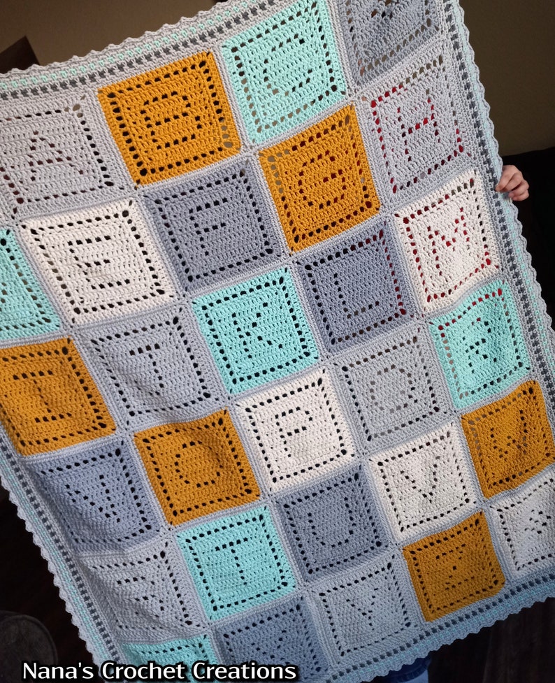 May include: A crocheted baby blanket with a square pattern in shades of gray, yellow, and teal. The blanket has a scalloped edge.