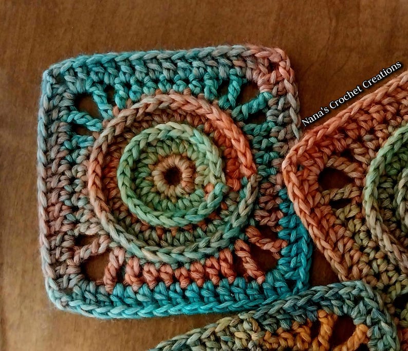 May include: A close-up of a crocheted square with a circular pattern in shades of teal, green, and peach. The square is part of a larger crocheted project.
