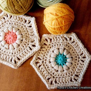 May include: Two crocheted hexagons with a flower design in the center. One flower is peach and the other is teal. The hexagons are beige and have a lacy border.