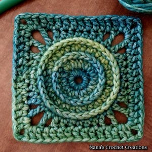 May include: A green, blue, and yellow crochet square with a circular design in the center. The square has a scalloped edge and is made with a variety of stitches.
