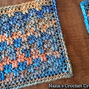 Könnte beinhalten: Zwei gehäkelte Quadrate in Blau-, Orange- und Brauntönen. Die Quadrate sind mit einem strukturierten Stich gearbeitet und haben einen Rand um die Kanten. "Nana's Crochet Creations" steht in der rechten unteren Ecke des Bildes.
