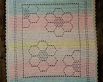 Könnte beinhalten: Eine pastellfarbene Häkeldecke für Babys mit einem gewellten Rand. Die Decke ist mit einem zarten Stichmuster gearbeitet und zeigt ein sich wiederholendes Muster aus kleinen Kreisen.