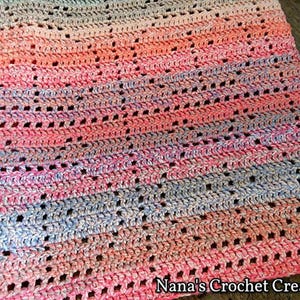 May include: A crocheted baby blanket in shades of pink, blue, and white with a lacy pattern. The blanket is made with a soft yarn and has a delicate, airy feel.