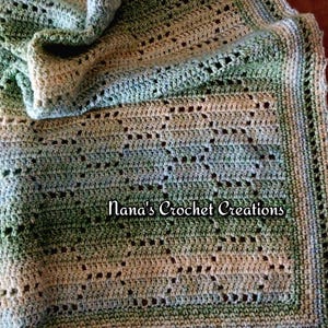 May include: A handmade crochet blanket featuring a variegated color palette of sage green, forest green, and cream. The textile displays an openwork geometric pattern with a decorative border. The text Nana's Crochet Creations is visible.