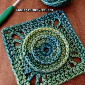 May include: A green and blue crochet square with a circular design in the center. The square has a textured, lacy pattern around the edges. "Nana's Crochet Creations" is written in white text on a brown background.