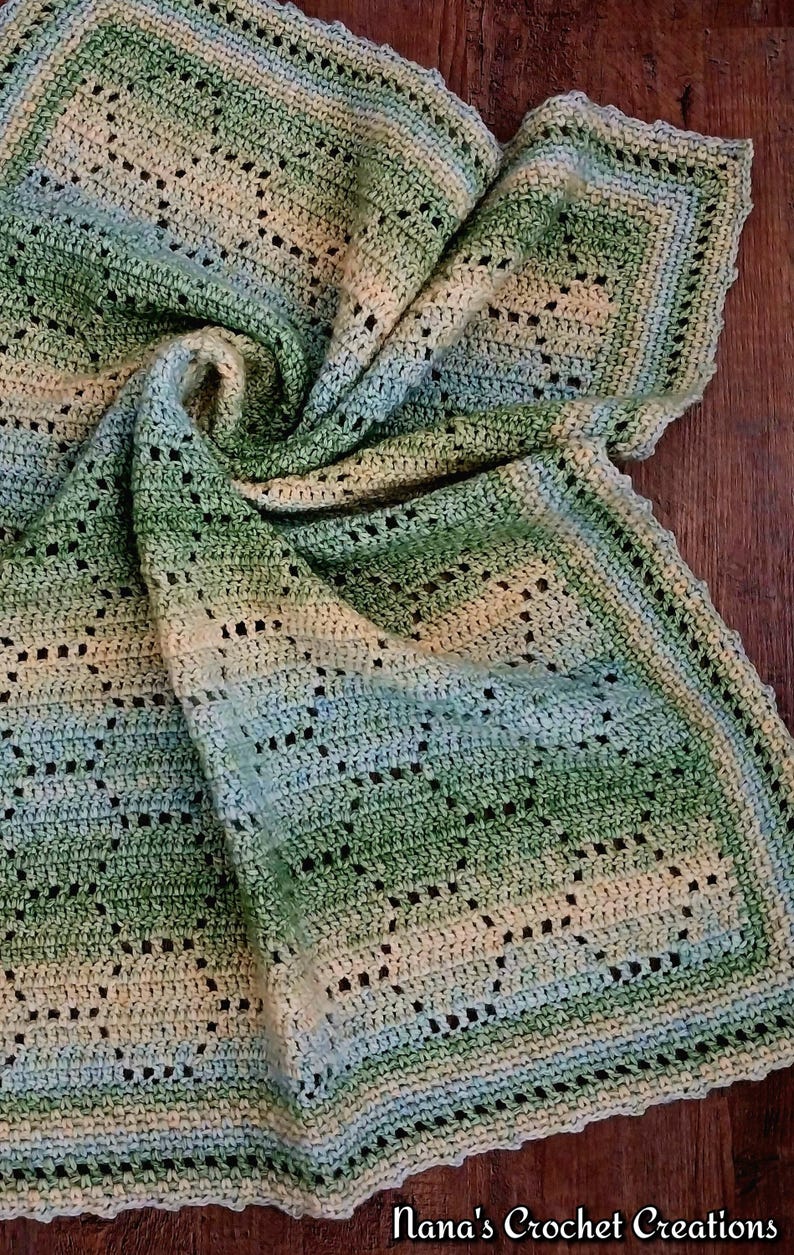 May include: A handmade crochet blanket featuring a gradient of green, cream, and light blue yarn. The textile displays an intricate openwork pattern with repeating geometric shapes and a scalloped border. The text Nana's Crochet Creations is visible.