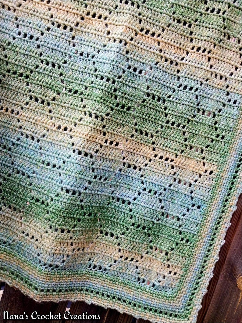 May include: A handmade crochet blanket featuring a repeating geometric pattern in a variegated color palette of soft green, pale blue, and cream. The textile has an openwork design with a finished border and the text Nana's Crochet Creations.