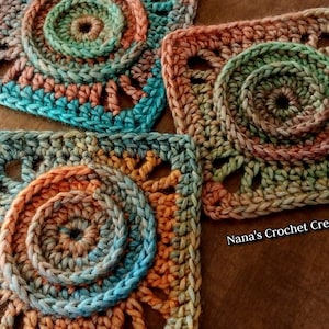 May include: Three crocheted squares with a multi-colored, circular pattern in shades of blue, green, orange, and brown. The squares are made with a textured stitch and have a lacy appearance. The text "Nana's Crochet Creations" is visible in the bottom right corner of the image.