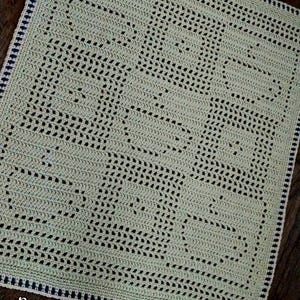 May include: A handmade, light green crochet blanket with a repeating openwork pattern. The blanket has a dark blue and white border and the text "Nana's Crochet Creations" at the bottom.
