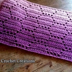 May include: A rectangular crochet scarf featuring an ombre gradient that transitions from light pink to deep purple. The fabric displays a repeating openwork geometric pattern throughout. The text Nana's Crochet Creations is printed in white.
