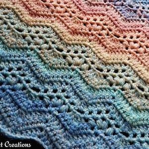 May include: A colourful crochet blanket with a chevron pattern in shades of blue, green, pink, and yellow. The blanket is made with a delicate stitch that creates a lacy effect.