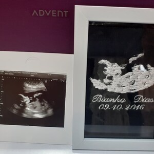 May include: A framed black and white ultrasound image of a baby in the womb. The frame has a white border and a silver inscription that reads "Bianka Dias 09.10.2016".