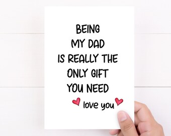 May include: A white greeting card with the text "BEING MY DAD IS REALLY THE ONLY GIFT YOU NEED" in black. Two red hearts and the words "love you" are below the text. The card is held by a hand.