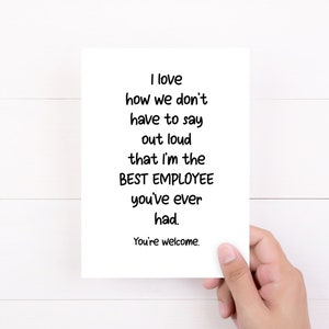 May include: A white rectangular greeting card featuring black text that reads: I love how we don't have to say out loud that I'm the BEST EMPLOYEE you've ever had. You're welcome. The card is held against a plain white background.