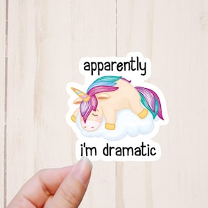 May include: A sticker featuring a cartoon unicorn with a rainbow mane and tail, sleeping on a cloud. The text "apparently i'm dramatic" is written below the unicorn.