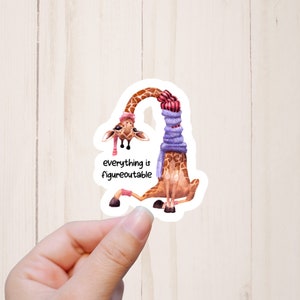 May include: A sticker featuring a cartoon giraffe wearing a purple scarf and a pink hat. The giraffe is sitting down with its legs crossed. The text "everything is figureoutable" is written below the giraffe.