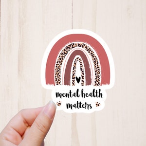 May include: A pink and brown rainbow sticker with a leopard print design. The sticker has a black heart in the center and the text "mental health matters" below it.