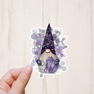 May include: A purple and white gnome sticker with a sparkly purple hat and holding a cluster of purple crystals. The gnome is surrounded by a white background with purple and white circles.