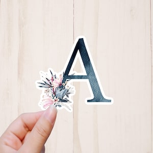 May include: A sticker with a blue watercolor letter A and a floral design with pink and blue flowers.