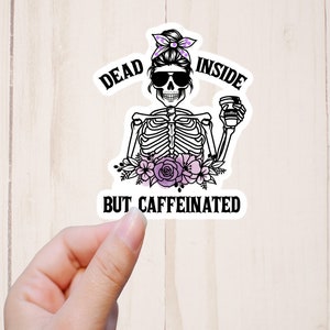 May include: A black and white sticker with a skeleton holding a coffee cup. The skeleton has a bun in its hair and sunglasses. The text on the sticker reads "Dead Inside But Caffeinated".