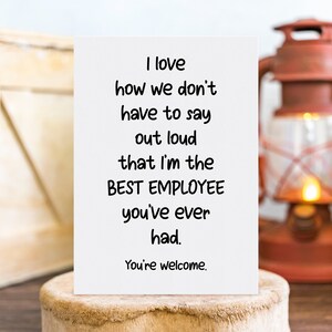 May include: A white greeting card with black text that reads: I love how we don't have to say out loud that I'm the BEST EMPLOYEE you've ever had. You're welcome. The card is rectangular and features a simple, clean design with bold lettering.