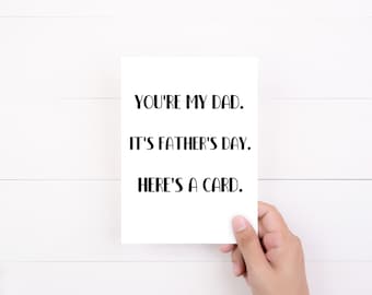May include: A rectangular white greeting card featuring black text that reads: YOU'RE MY DAD. IT'S FATHER'S DAY. HERE'S A CARD. The card has a clean, simple design with bold, sans-serif lettering centered on the front surface of the paper.