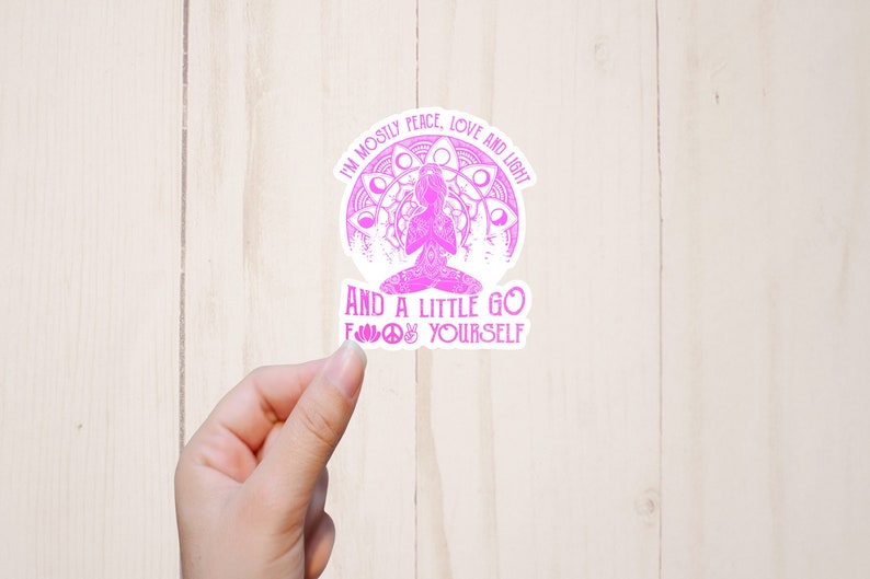 Może przedstawiać: R&oacute;żowa i biała naklejka z napisem "I'm mostly peace, love and light" i "And a little go f*** yourself". Naklejka przedstawia medytującą postać i wz&oacute;r mandali.