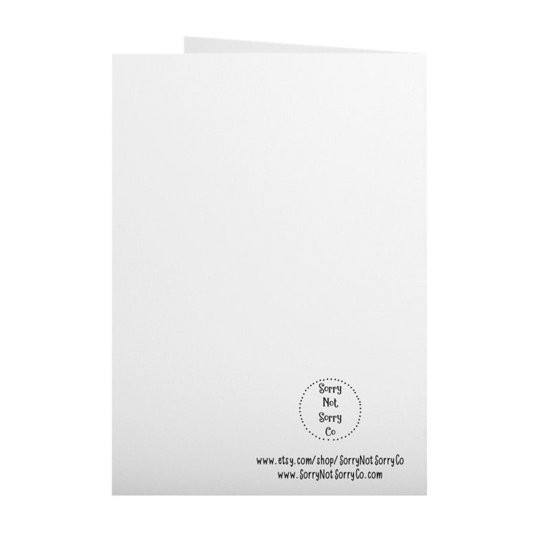 May include: A folded white greeting card with the text "Sorry Not Sorry Co" in a circular design at the bottom right. Below the design are two lines of text with a website address.