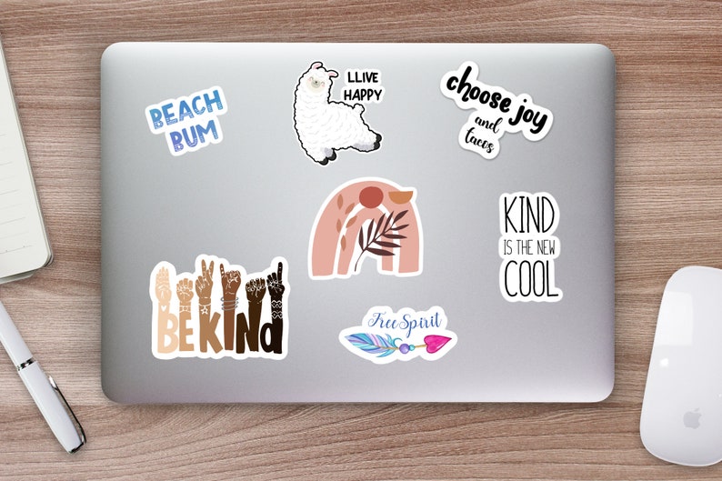 K&ouml;nnte beinhalten: Ein Laptop-Computer mit mehreren Aufklebern. Die Aufkleber zeigen verschiedene Designs und S&auml;tze, darunter ein Lama, ein Regenbogen, eine Feder und die Worte "Beach Bum", "Live Happy", "Choose Joy and Tacos", "Be Kind", "Kind is the New Cool" und "Free Spirit".