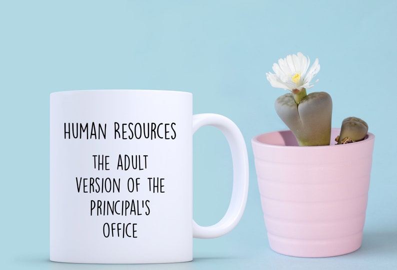 May include: White ceramic mug with the text "HUMAN RESOURCES THE ADULT VERSION OF THE PRINCIPAL'S OFFICE" in black. A small pink pot with a succulent plant and white flower sits to the right. The background is light blue.