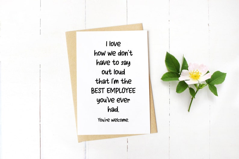 May include: A white greeting card with black text that reads: I love how we don't have to say out loud that I'm the BEST EMPLOYEE you've ever had. You're welcome. The card is placed on top of a tan envelope, accompanied by a single white and pink flower.