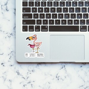 May include: A pink flamingo with a glass of wine in its hand, with the text "MY SPIRIT ANIMAL" below it. The sticker is on a silver laptop.