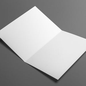 Op de afbeelding: Een opengevouwen witte kaart ligt op een grijze ondergrond. De kaart is in een hoek geplaatst, waardoor de binnenkant en de scherpe randen van het papier zichtbaar zijn. Geschikt voor uitnodigingen.