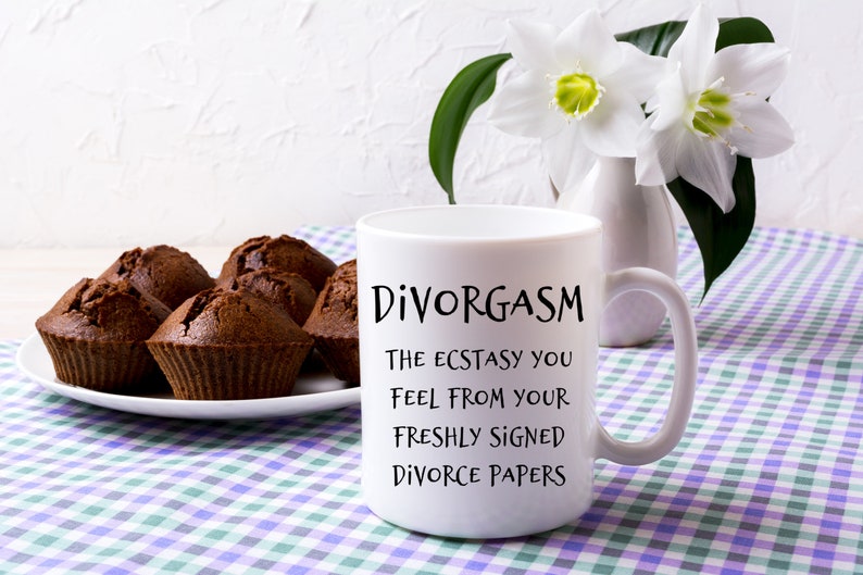 Puede incluir: Taza de caf&eacute; blanca con texto negro que dice "Divorgasm The Ecstasy You Feel From Your Freshly Signed Divorce Papers". La taza est&aacute; sobre un mantel a cuadros con magdalenas de chocolate en un plato blanco en el fondo.