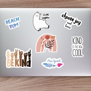 May include: A laptop computer with several stickers on it. The stickers feature various designs and phrases, including a llama, a rainbow, a feather, and the words "Beach Bum", "Live Happy", "Choose Joy and Tacos", "Be Kind", "Kind is the New Cool", and "Free Spirit".
