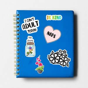 May include: A blue notebook with a spiral binding and several colorful stickers. The stickers feature phrases like "I can't adult today", "Be Kind", "Naps", and "Keep glowing". There is also a sticker of a jar with a firefly inside and a sticker of pink flowers.