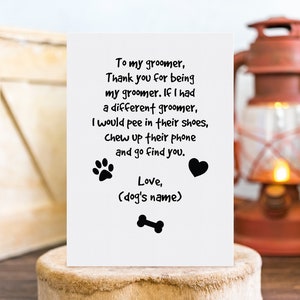 May include: A white greeting card with black text, paw prints, a heart, and a bone illustration. The card's message is a humorous thank you to a dog groomer. The card is displayed on a wooden surface.