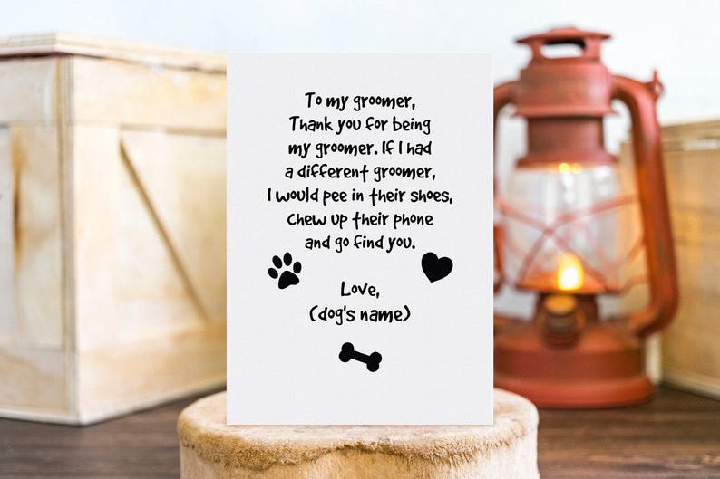May include: A white greeting card with black text, paw prints, a heart, and a bone illustration. The card's message is a humorous thank you to a dog groomer. The card is displayed on a wooden surface.
