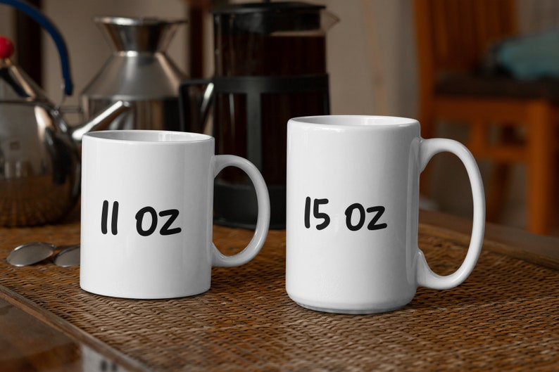 Puede incluir: Dos tazas de cer&aacute;mica blanca con letras negras. La taza de la izquierda dice "11 oz" y la taza de la derecha dice "15 oz".