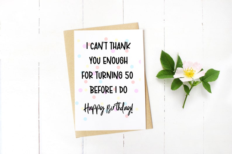 Może przedstawiać: Kartka urodzinowa z napisem "I can't thank you enough for turning 50 before I do. Happy Birthday!". Kartka leży na białej powierzchni, wraz z kopertą z papieru kraft i gałązką kwiatową.