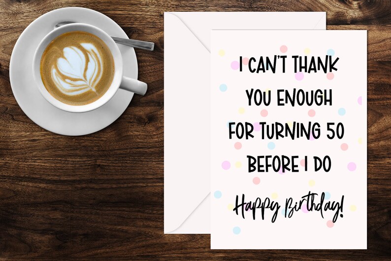 Może przedstawiać: Karta urodzinowa z napisem "I can't thank you enough for turning 50 before I do. Happy Birthday!" jest wyświetlana obok białej koperty. Filiżanka kawy z latte art stoi na spodku z łyżeczką.